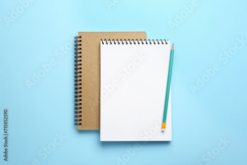 Notebooks and pencil on light blue background, top view