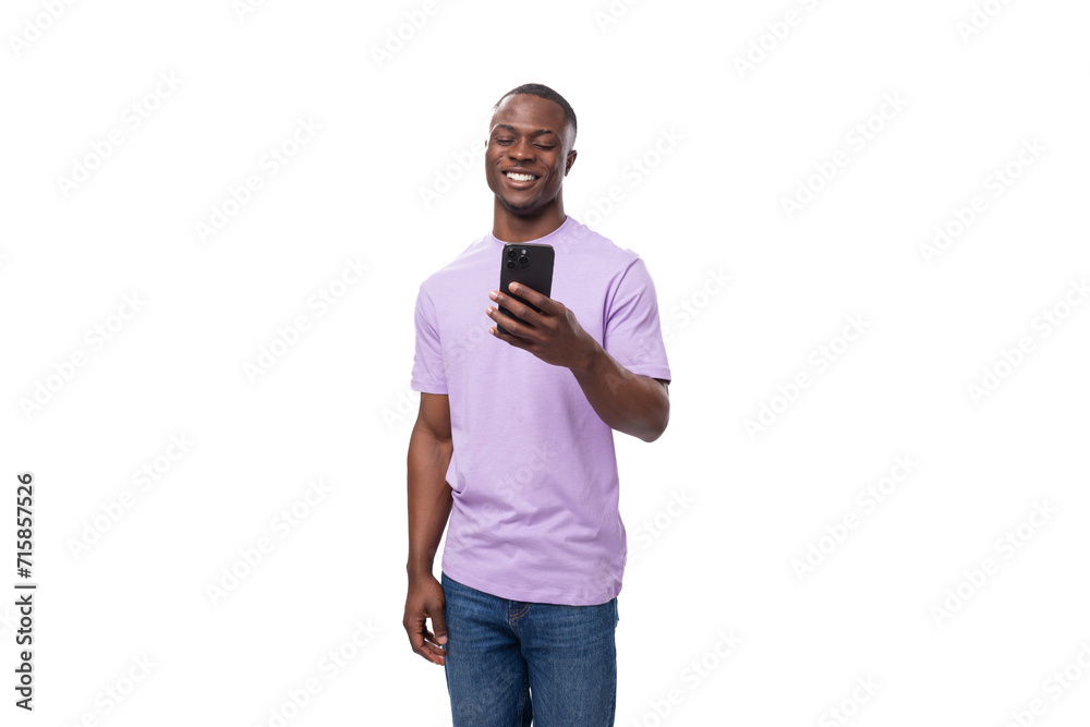 young smart african man dressed in a lilac t-shirt and jeans uses a smartphone young smart african man dressed in a lilac t-shirt and jeans uses a smartphone