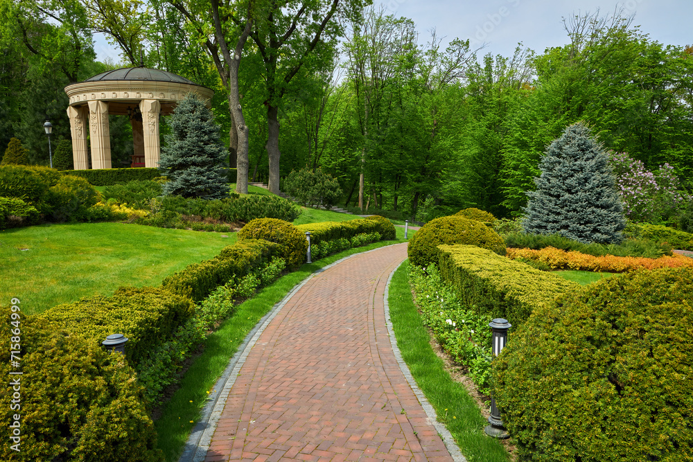Fototapeta premium Trimmed green bushes form a labyrinth along tiled pathways in the park,