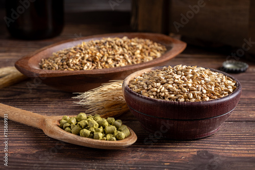 Barley in wooden bowl and granulated hops in a wooden spoon on a wooden table. Ingredients for craft beer.