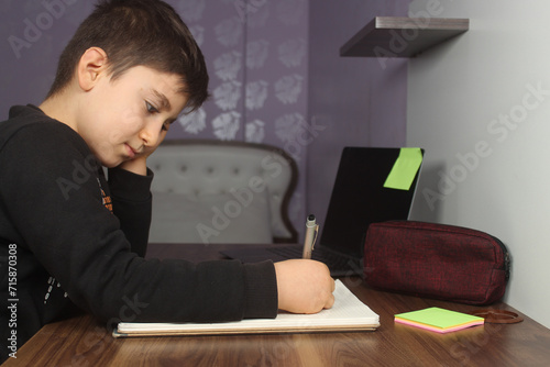 Distance learning online education. A schoolboy boy studies at home and does school homework. Bored student trying to write a composition. Stay at home concept idea.  photo