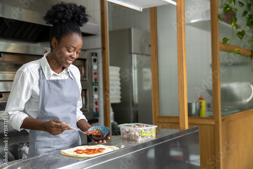 Smiling dark-skinned woman preparing pizza and looking contented photo