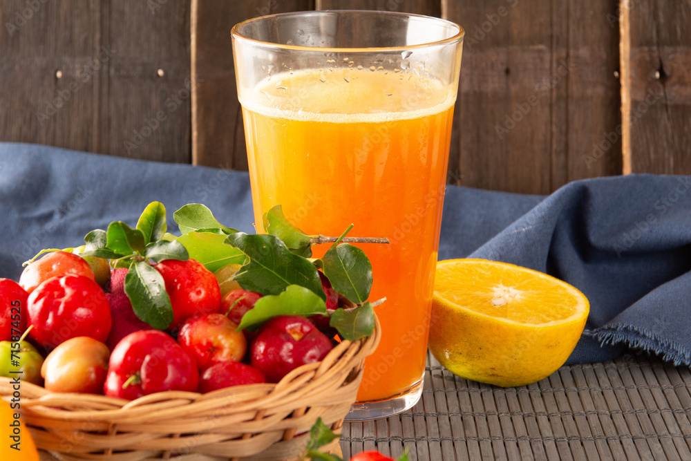 Fresh acerola juice in a glass cup in a bamboo place mat with sliced oranges and acerola fruits front view Fresh acerola juice in a glass cup in a bamboo place mat with sliced oranges and acerola fruits front view