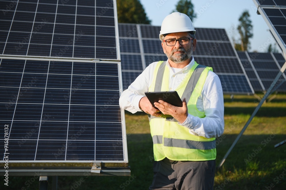 Elderly engineer is checking with tablet an operation of sun and cleanliness on field