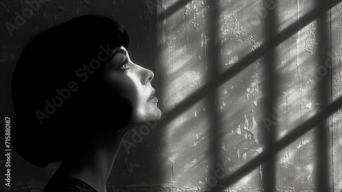 Contemplative woman by window with light and shadows in monochrome