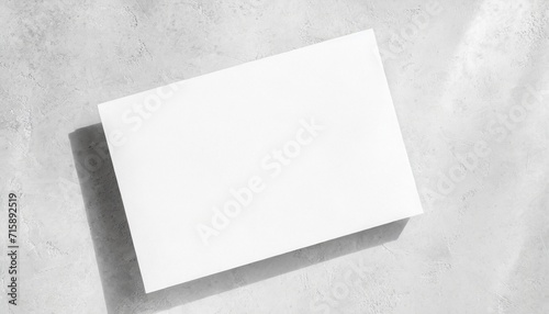 closeup of empty white rectangle poster mockups lying diagonally with soft shadow on neutral light grey concrete background flat lay top view open composition photo