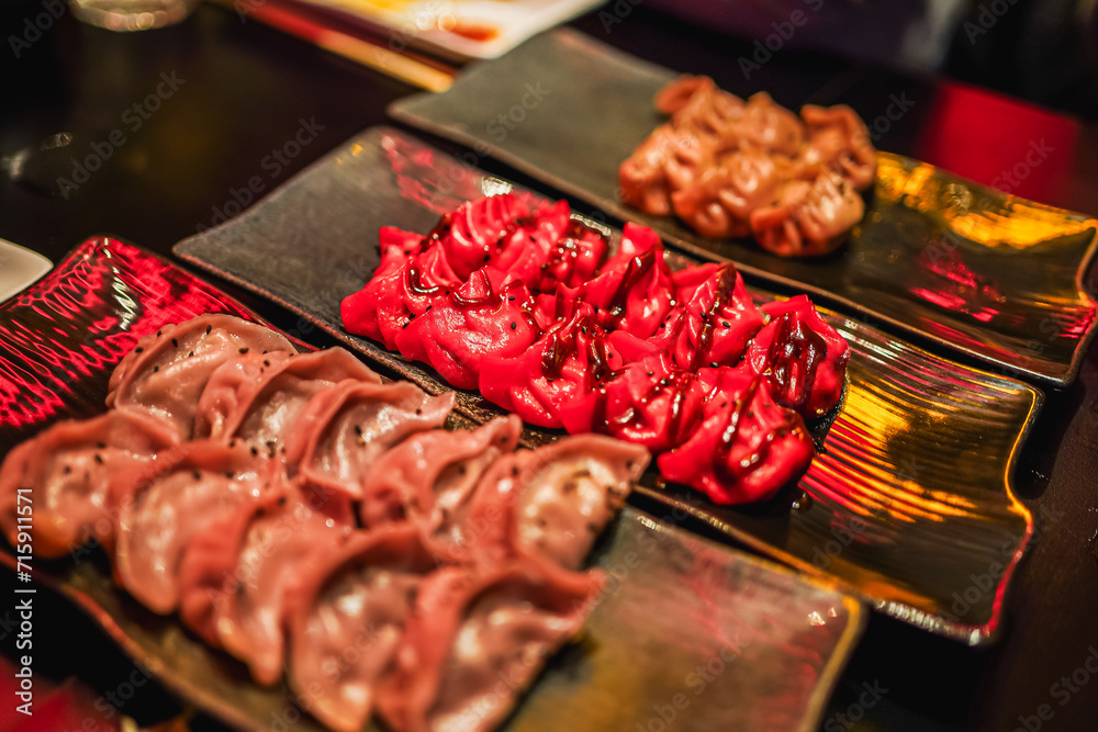 Vibrant red and brown gyozas on a black plate, ready to be enjoyed in a dimly lit setting. Vibrant red and brown gyozas on a black plate, ready to be enjoyed in a dimly lit setting.
