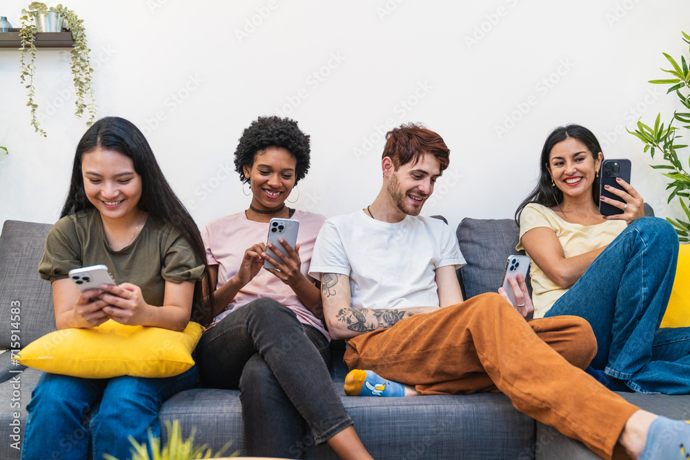 Four happy friends enjoying social media on their phones, sharing laughs on a comfortable sofa together Four happy friends enjoying social media on their phones, sharing laughs on a comfortable sofa together