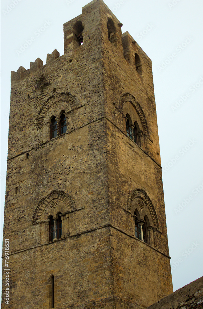Close-up view upper part of stone belltower of ancient Erice Cathedral in small mountain village Erice. Notable landmark of Sicily. Travel and tourism concept. Cloudy sky background
