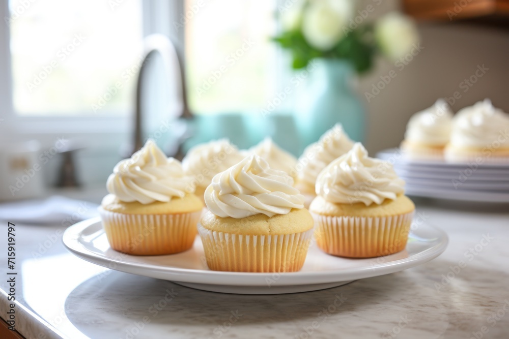  a plate of cupcakes with white frosting on top of a kitchen counter with plates of cupcakes in the background.
