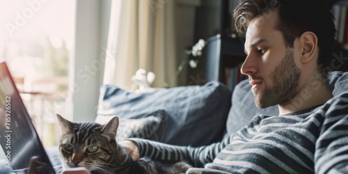 Handsome man working online from home by cat pet accompanied on his laptop