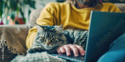Handsome man working online from home by cat pet accompanied on his laptop