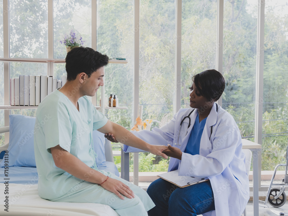 Portrait patient caucasian man with woman nurse carer physical therapist African-American two people sitting talk helping support give advice and holding hand arm inside hospital indoor room service. Portrait patient caucasian man with woman nurse carer physical therapist African-American two people sitting talk helping support give advice and holding hand arm inside hospital indoor room service.