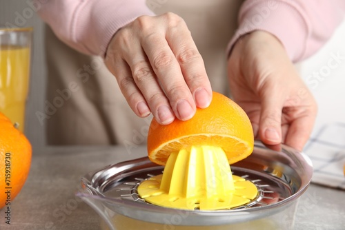 Woman squeezing orange juice at grey table, closeup photo