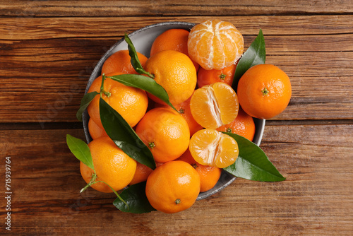 Fresh tangerines with green leaves in bowl on wooden table, top view