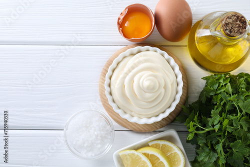 Fresh mayonnaise sauce in bowl and ingredients on white wooden table, flat lay. Space for text