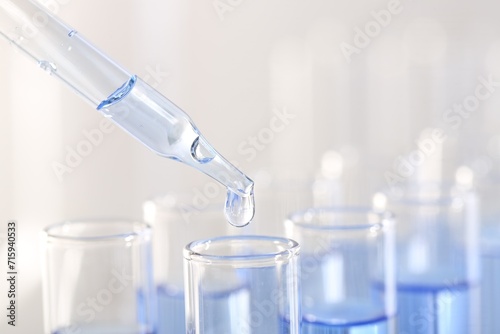 Laboratory analysis. Dripping light blue liquid from pipette into glass test tube on blurred background, closeup