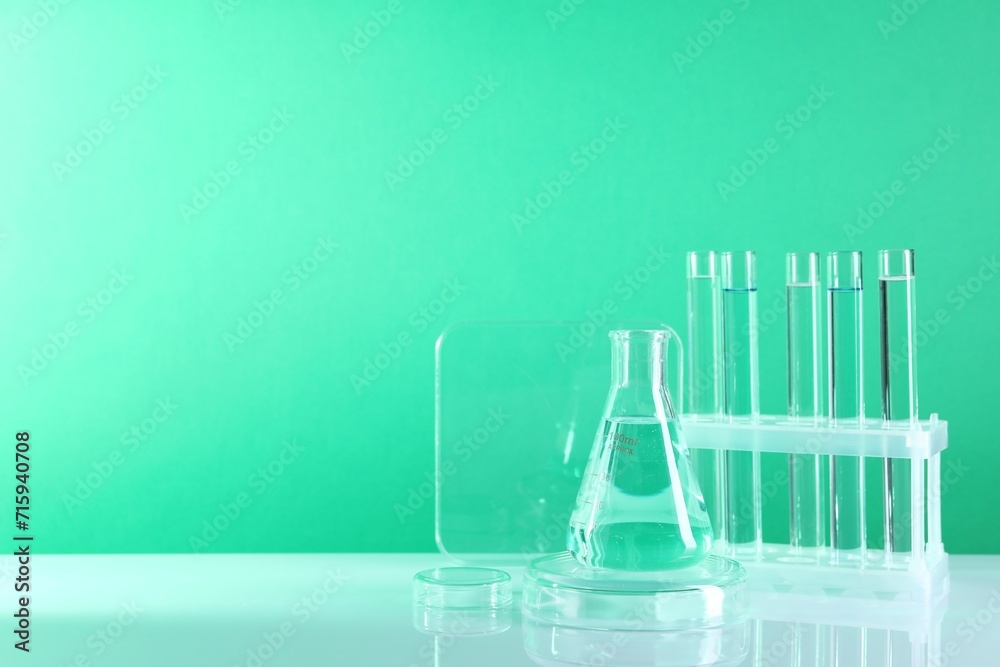 Laboratory analysis. Different glassware on table against green background, space for text Laboratory analysis. Different glassware on table against green background, space for text