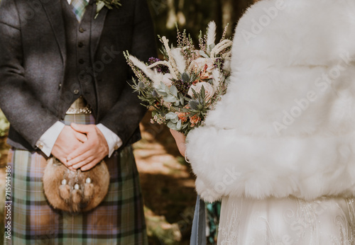 Bride and Groom in a kilt stand outdoors at a wedding ceremony about to be married in Scotland