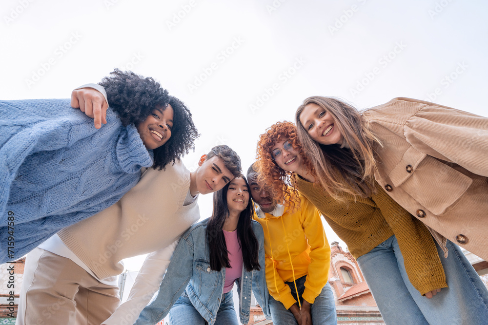 Cheerful young friends leaning forward for a group photo under a clear sky, exuding warmth and camaraderie