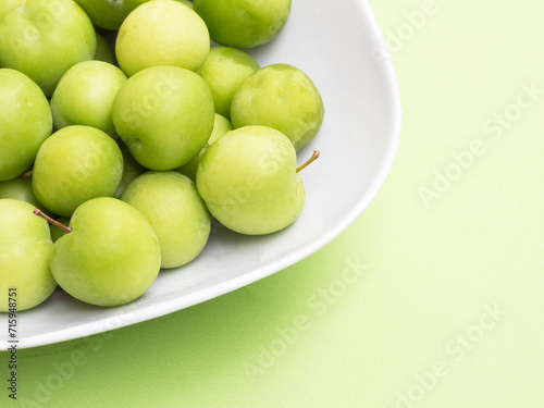 group of green plums in white bowl on green background. fresh green plum