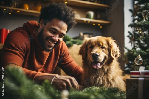Portrait of a handsome young African American man and cute dog in Christmas setting. Cheerful guy and his adorable pet are preparing for holidays, decorating Christmas tree and having fun.