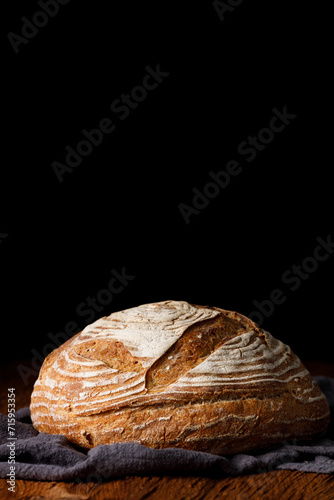 Rustic sourdough wheat bread on a wooden table and dark background. Photo front.