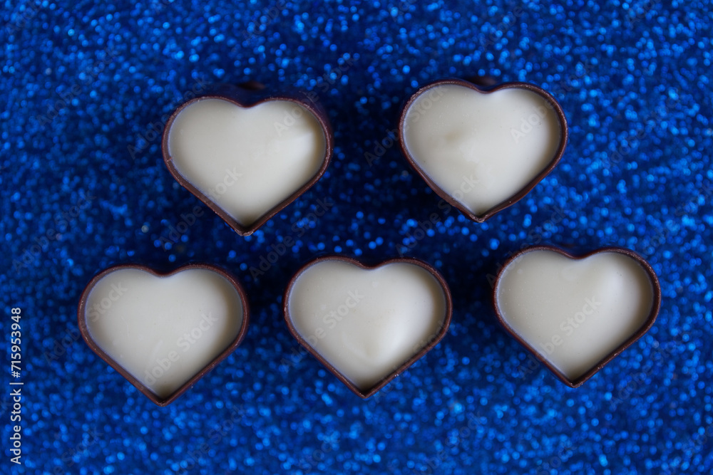 Five heart-shaped dark and white chocolate candies in dark and white chocolate. Festive blue shimmery background. Romantic concept. Photo. Bokeh. Selective focus