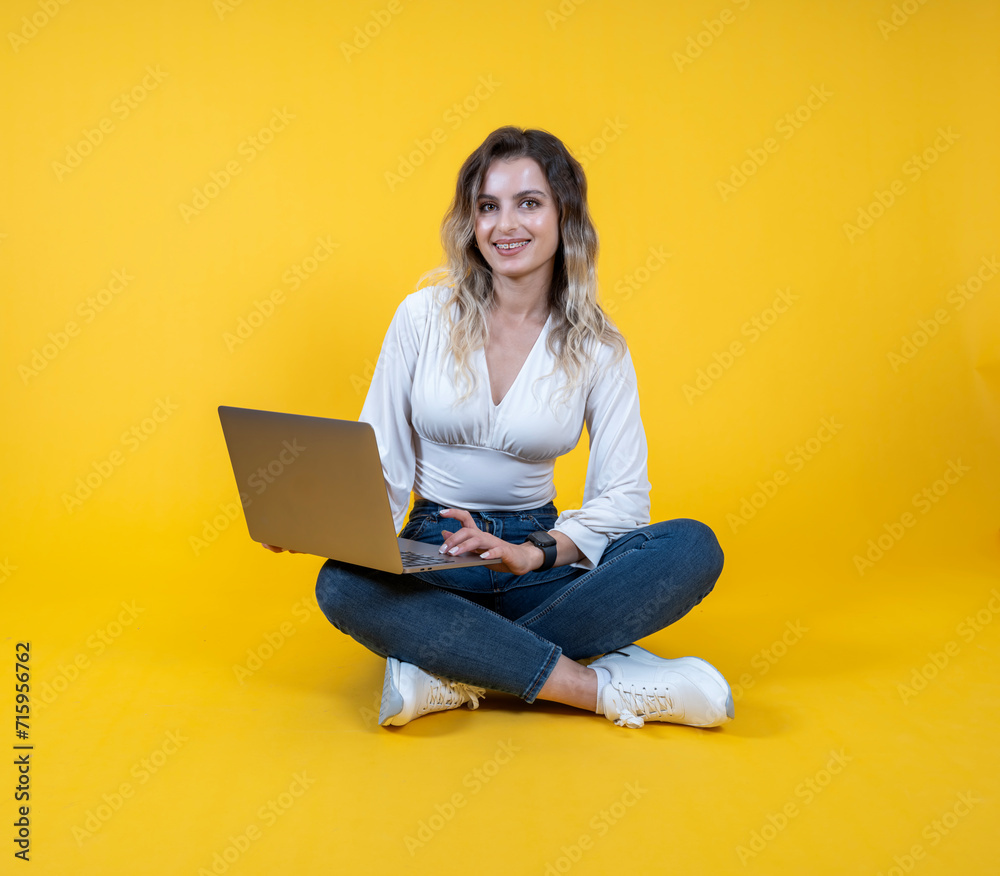 Naklejka premium Woman hold use laptop, full body young cheerful caucasian woman hold use laptop. Sit floor legs crossed. Wearing white shirt, causal denim jeans white sneakers. People lifestyle concept. 