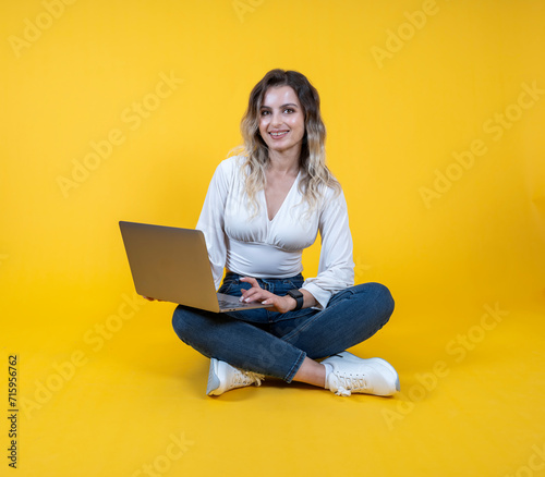 Woman hold use laptop, full body young cheerful caucasian woman hold use laptop.  Sit floor legs crossed. Wearing white shirt, causal denim jeans white sneakers. People lifestyle concept.  © Designerant