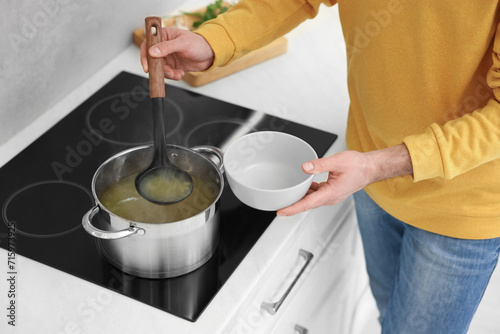 Man pouring delicious soup into bowl in kitchen, closeup