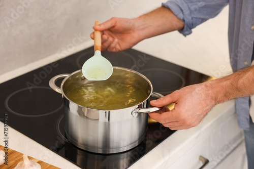 Man cooking delicious chicken soup in kitchen, closeup
