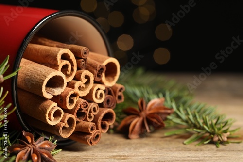 Many cinnamon sticks, anise stars and fir branches on wooden table, closeup. Space for text