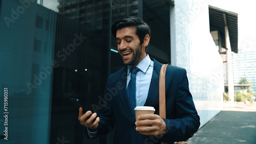 Smart manager looking at mobile phone and walking at street while wearing suit. Skilled investor looking mobile phone to checking sales or working while holding coffee cup. White background. Exultant. photo