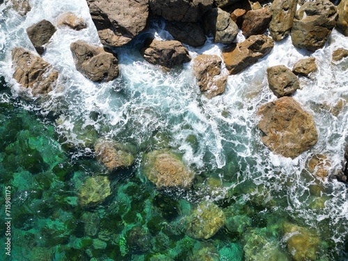 Graphic artistic aerial shot of the sea crashing over rocks on the North Cornwall coastline. Clear turquoise seas and white waves near Port Isaac.