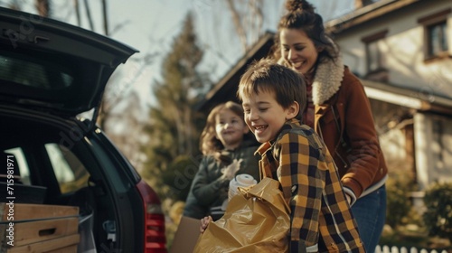 Happy young family with little packing stuff into the car and smiling while standing near house