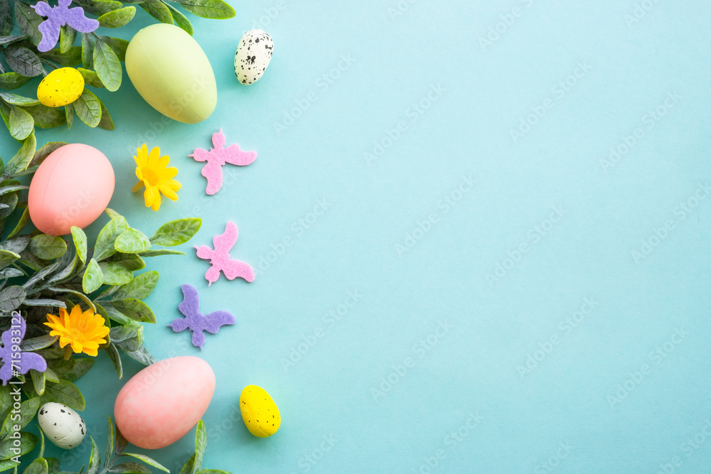 Easter background or greeting card on blue. Eggs, spring leaves, flowers and colored butterflies. Flat lay with copy space.