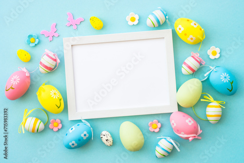 Easter background on blue. Colored easter eggs with decorations and white frame for text. Flat lay with copy space.