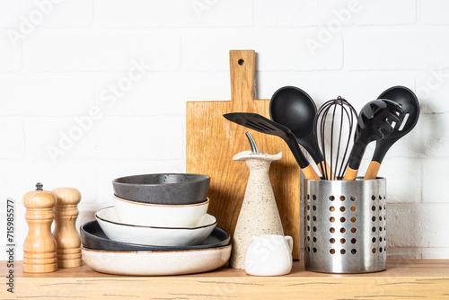Kitchen table, kitchen utensils, plates, bowls, shakers and wooden cutting board, white modern interior. Modern kitchen interior.