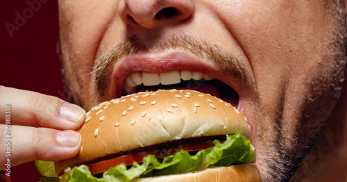 Close up of man eating hamburger with his mouth wide open.