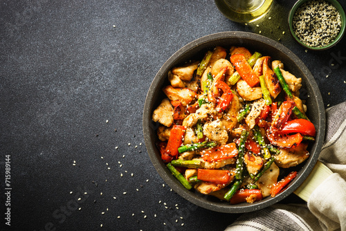 Chicken stir fry with vegetables in the skillet at black stone background. Top view with copy space.