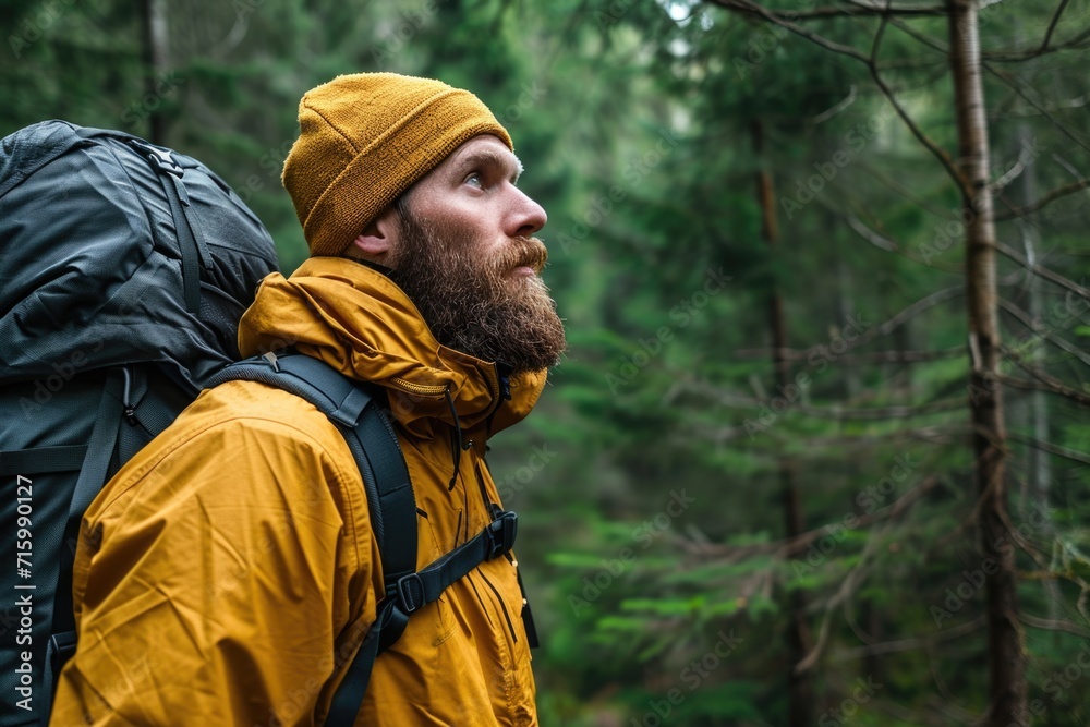 Contemplative bearded man wearing a yellow raincoat while hiking in a lush forest