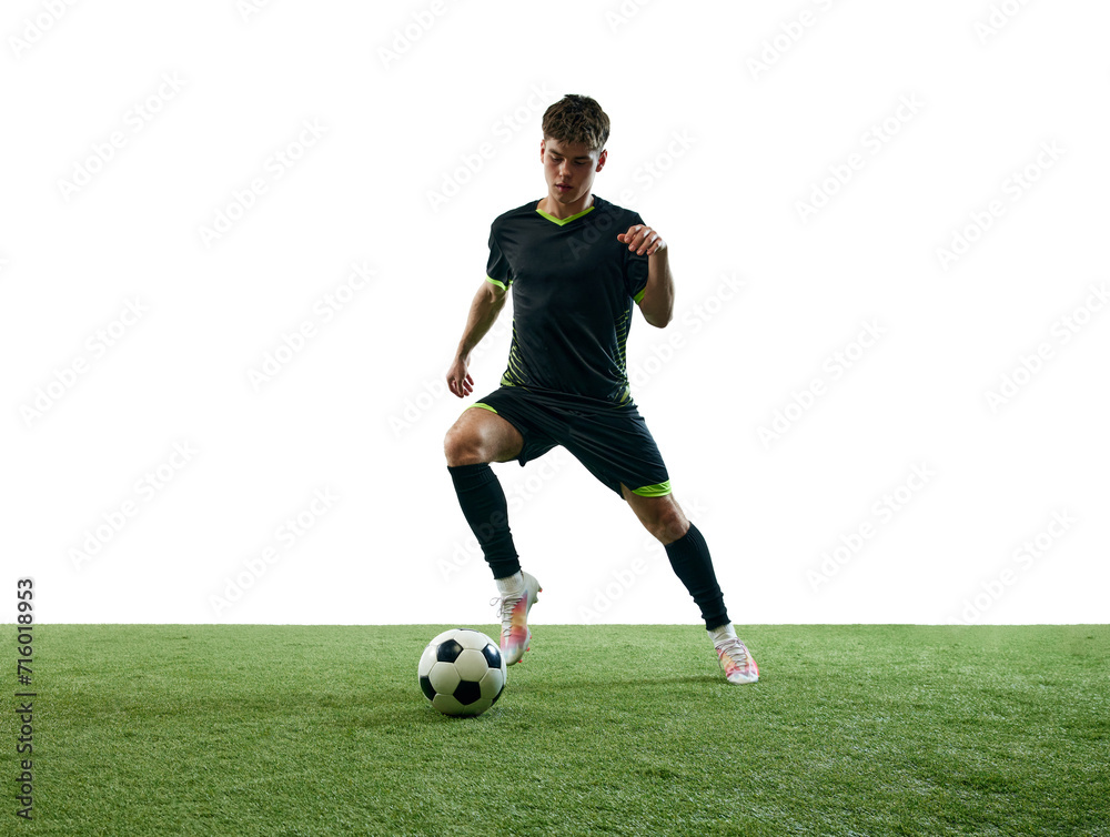 Young man in black uniform, soccer player playing, dribbling ball isolated over white background with grass flooring. Concept of sport, game, competition, championship, active lifestyle