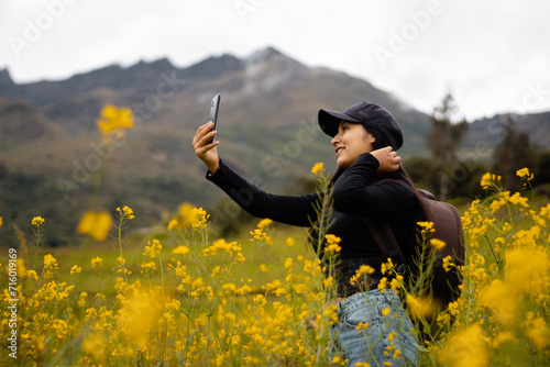 Una chica turista  con mochila , gorra y celular en el paraíso floral, Encanto primaveral, tecnología y flores amarillas en armonía.