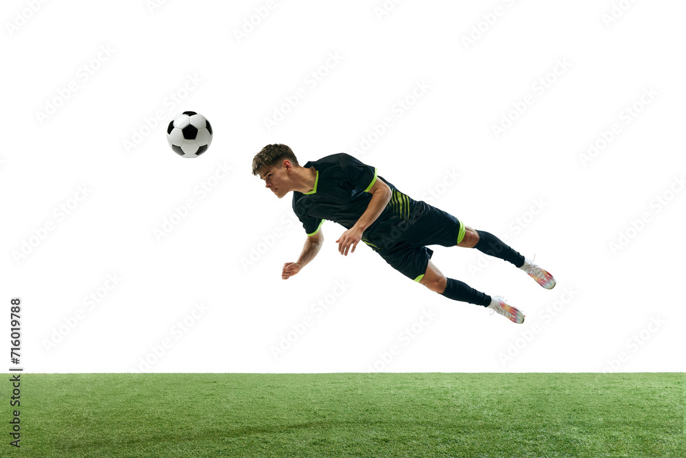 Dynamic image of young man, football player in motion, hitting ball with head isolated over white background with grass flooring. Concept of sport, game, competition, championship, active lifestyle