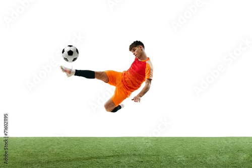 Champion. Young guy, soccer player in orange uniform training, hitting ball with leg isolated over white background with grass flooring. Concept of sport, competition, championship, active lifestyle