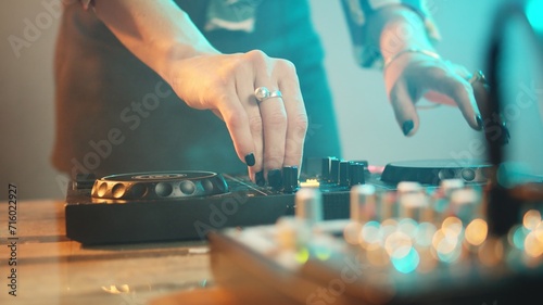 Young performer using dj electronics and headset to mix techno music and play remix songs on turntables, having fun at nightclub. Woman with crazy makeup mixing instruments. Close up. Handheld shot.
