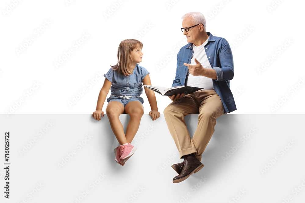 Obraz premium Mature man holding a book and talking to a little girl