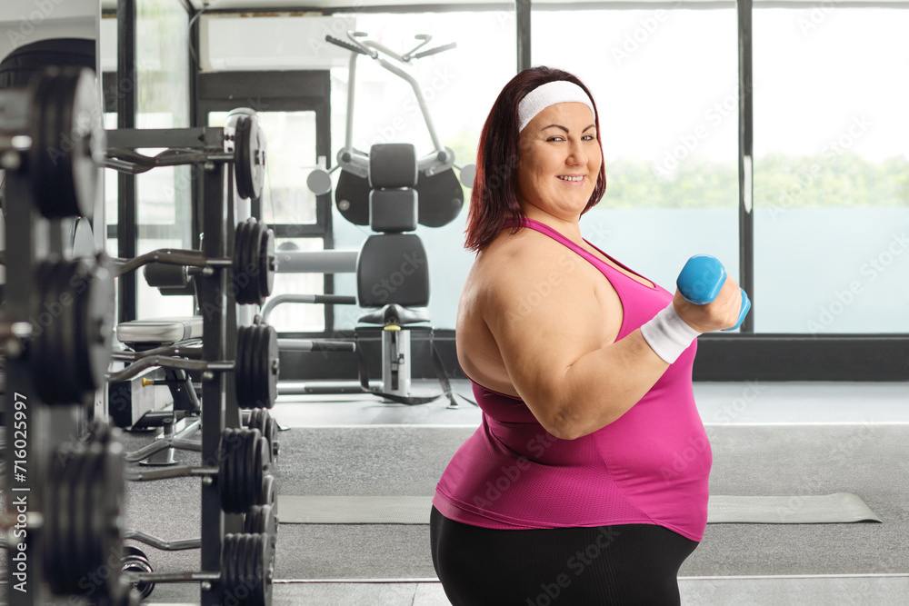 Corpulent woman exercising with a dumbbell and smiling Corpulent woman exercising with a dumbbell and smiling