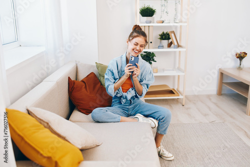 Happy woman holding mobile phone and smiling while relaxing on a cozy sofa at home